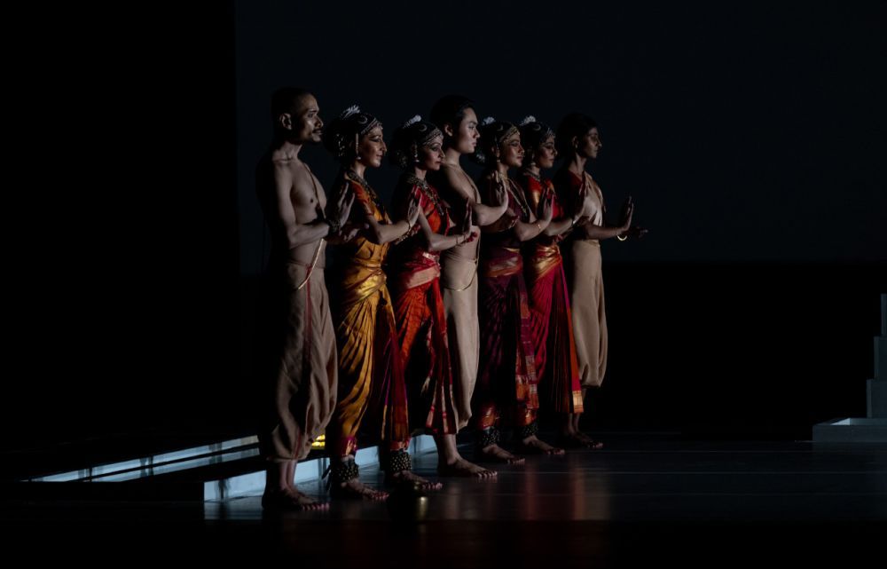 Several dancers stand in a line on stage ready to perform.