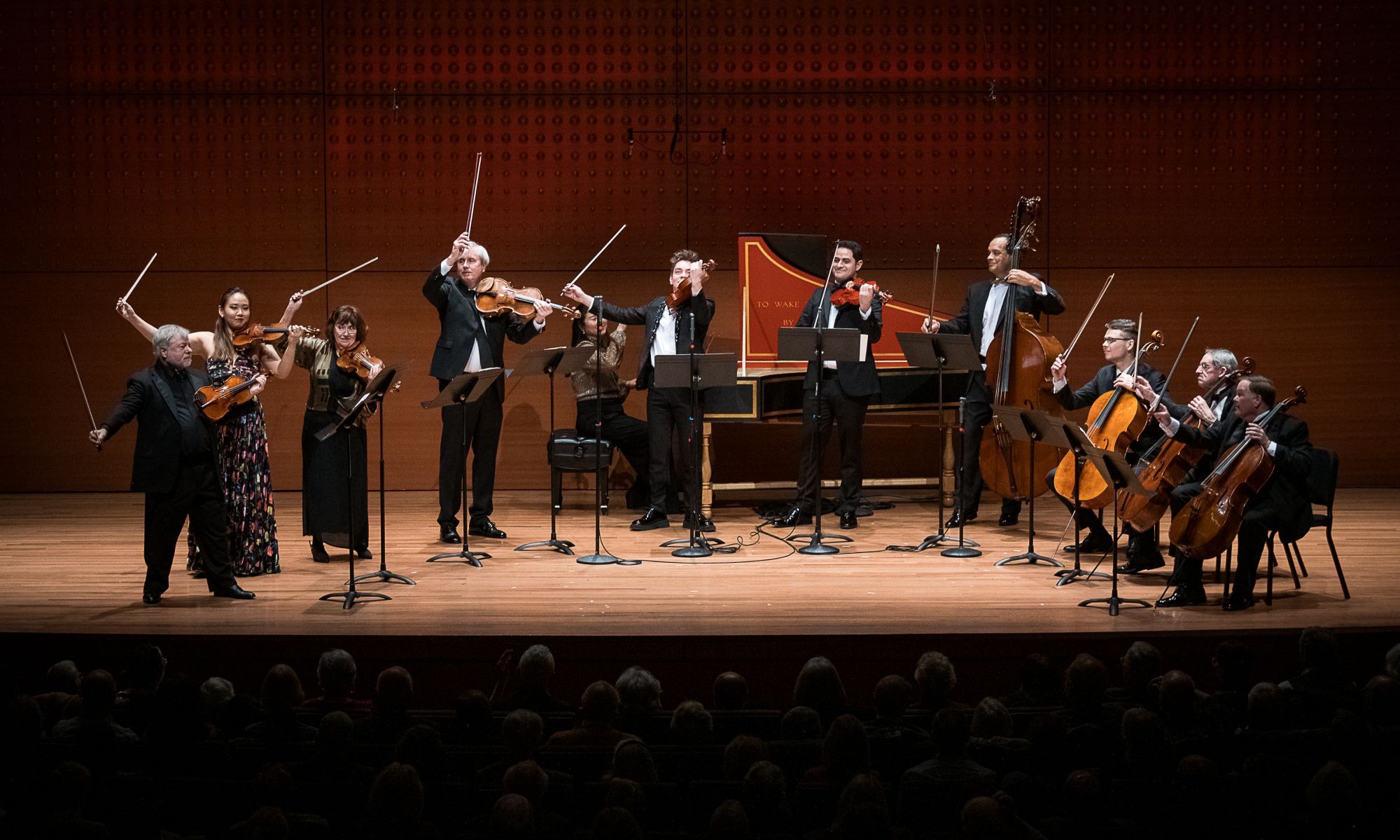 An ensemble of musicians on stage lifting their bow's as if they are finished playing.