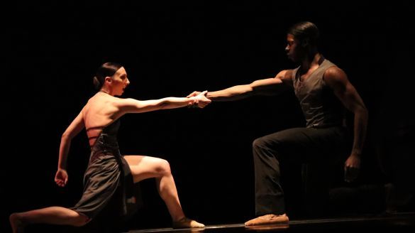 Two Giordano Dance Chicago Dancers kneel on one knee facing each other and holding opposite hands.